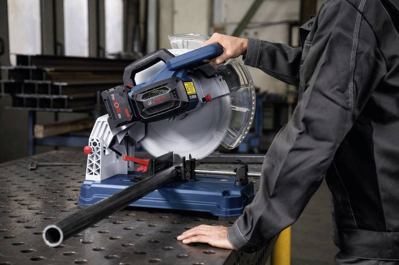 Eine Person schneidet mit einer Metallkappsäge ein Metallrohr in einer Werkstatt.