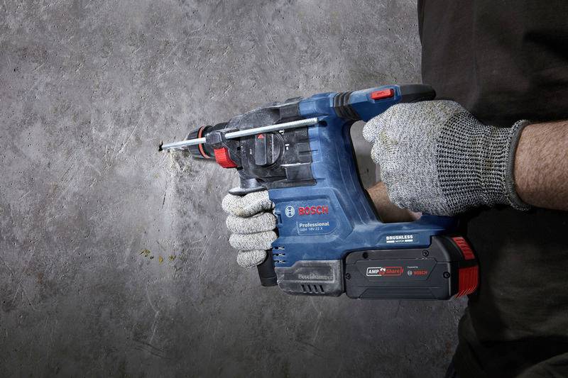 Eine Person bohrt mit einem blauen Bosch-Bohrhammer in eine Betonwand. Die Person trägt Sicherheitshandschuhe.