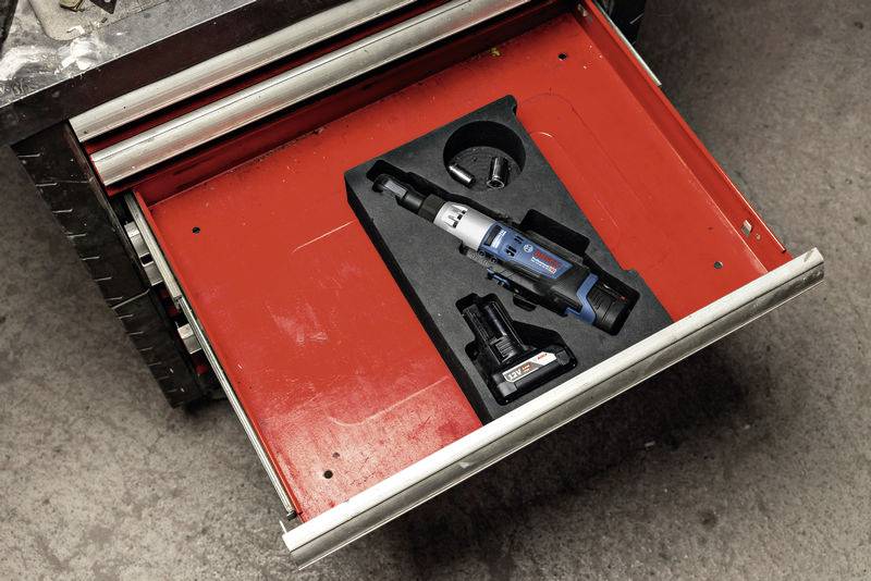 Eine geöffnete Werkzeugschublade enthält einen elektrischen Schraubendreher mit Akku und Ladestation auf rotem Hintergrund.