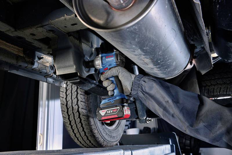 Eine Person mit grauen Handschuhen arbeitet unter einem Fahrzeug, verwendet einen blauen Akku-Schlagschrauber, um Teile zu befestigen.