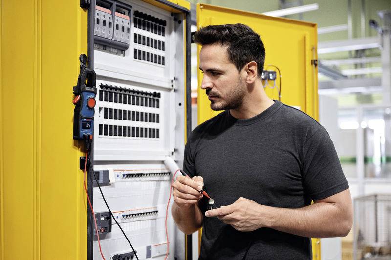 Ein Mann arbeitet an einem geöffneten Schaltschrank. Er hält ein Werkzeug und überprüft die elektrischen Komponenten im Inneren.