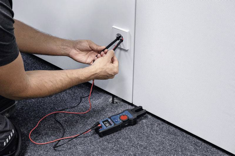 Eine Person testet mit einem Multimeter die Spannung an einer Steckdose.