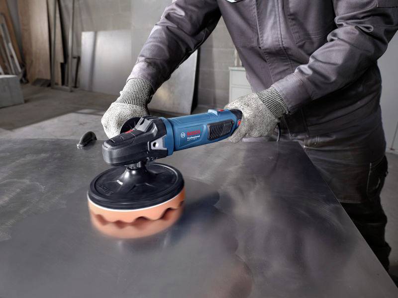 Person poliert eine Metalloberfläche mit einer elektrischen Poliermaschine in einer Werkstattumgebung.