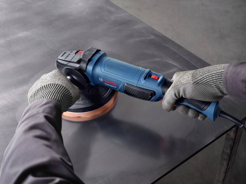 Eine Person schleift mit einem elektrischen Winkelschleifer eine Metalloberfläche. Sie trägt Arbeitshandschuhe.