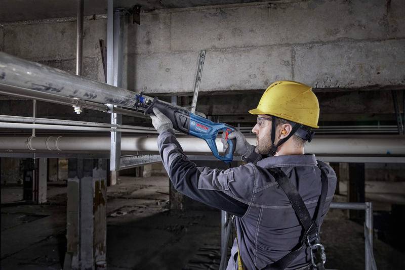 Ein Bauarbeiter mit Schutzhelm verwendet eine elektrische Säge, um ein Metallrohr in einem Gebäude zu schneiden.