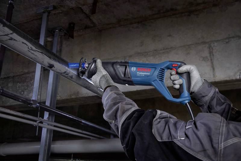 Eine Person schneidet ein Metallrohr mit einer blauen Bosch-Stichsäge in einem industriellen Umfeld. Arbeitet präzise an der Rohrleitung.