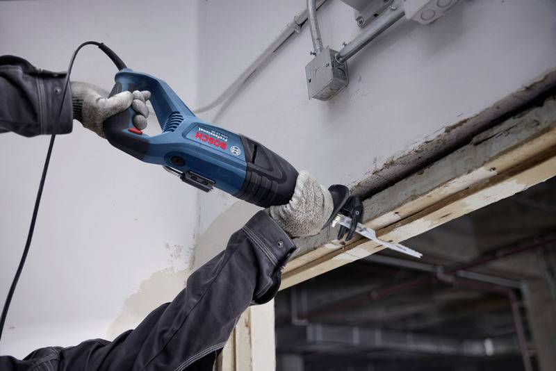 Eine Person verwendet eine Elektrosäge, um einen Türrahmen zu schneiden. Die Umgebung wirkt wie eine Baustelle.