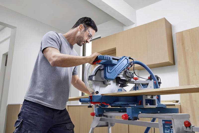 Ein Mann arbeitet in einer Werkstatt mit einer Kreissäge, um ein Holzbrett zu schneiden. Er trägt eine Schutzbrille.