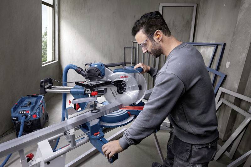 Ein Mann bedient eine Kreissäge in einer Werkstatt. Er trägt Sicherheitsbrille und Gehörschutz. Die Umgebung wirkt industriell und modern.