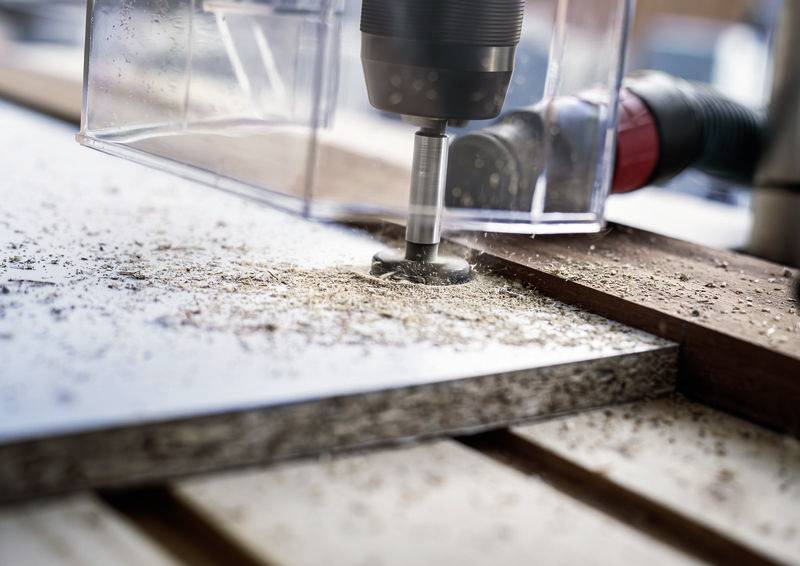 Nahaufnahme einer Bohrmaschine, die ein Loch in ein Holzbrett bohrt. Holzspäne spritzen herum.