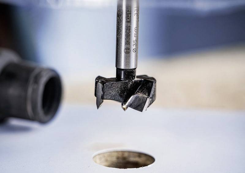 Ein Bohrer mit scharfer Schneide in Bewegung, nah an einem gebohrten Loch in einer Metalloberfläche, mit unscharfem Hintergrund.