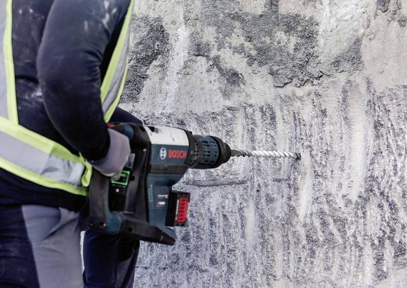 Person in Arbeitskleidung bohrt mit einer Bosch-Bohrmaschine in eine graue Betonwand.