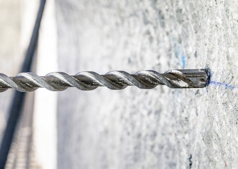 Ein Bohrer dringt in eine Betonwand ein. Die Nahaufnahme zeigt den spiralförmigen Bohrkopf und die raue Textur der Wand.