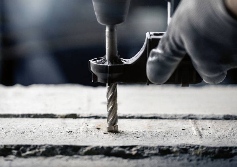 Eine Hand mit einem Handschuh hält eine Bohrmaschine, die ein Loch in eine Betonoberfläche bohrt.