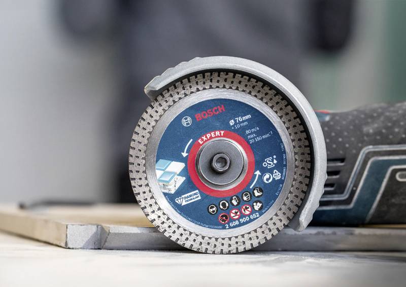 Ein Winkelschleifer mit einer Diamantscheibe, markiert mit Logos und Spezifikationen, liegt auf einer Werkbank.