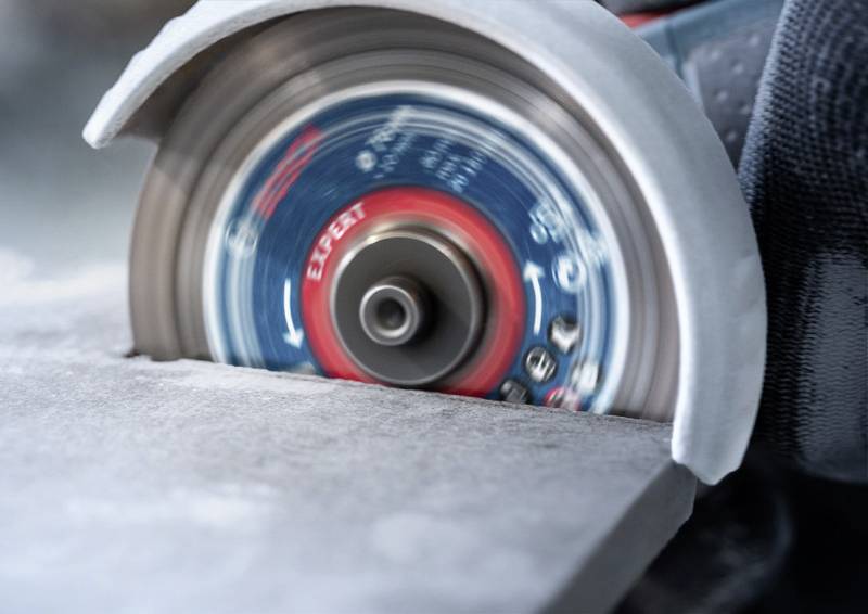 Eine Kreissäge schneidet präzise durch eine Steinplatte. Die rotierende Scheibe ist in Bewegung und erzeugt feinen Staub.