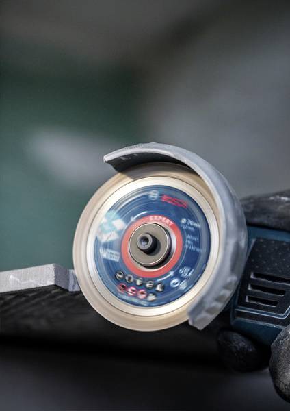 Eine Schleifmaschine bearbeitet eine Metallkante, funkenloser Einsatz. Fokus auf die rotierende Schleifscheibe im Betrieb.