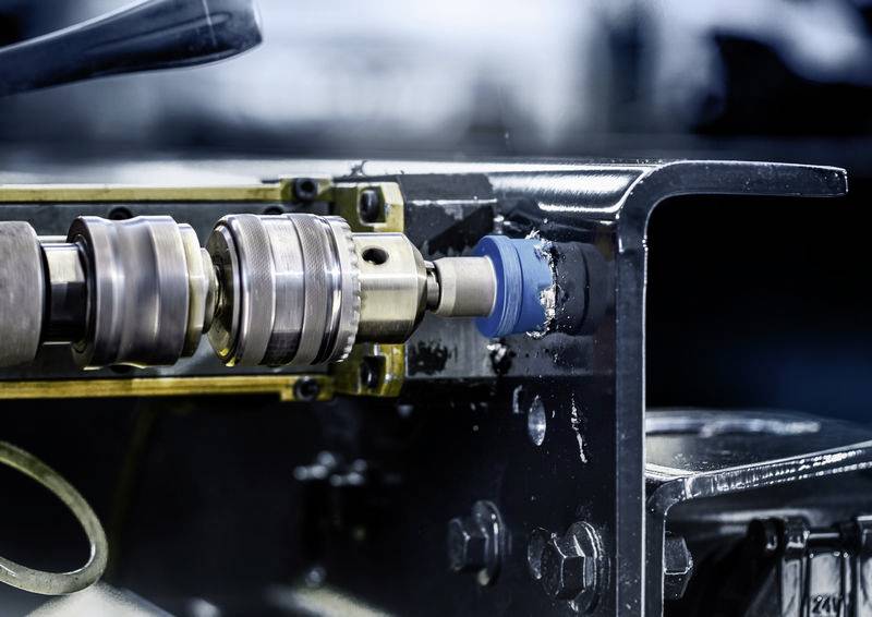 Ein Bohrwerkzeug bearbeitet ein Metallteil, das in einer Werkstatt eingespannt ist. Es dreht sich schnell und erzeugt Späne.