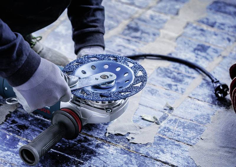 Person arbeitet mit Winkelschleifer auf blauem Bodenbelag, trägt Sicherheitshandschuhe. Reparatur- oder Renovierungsarbeiten.