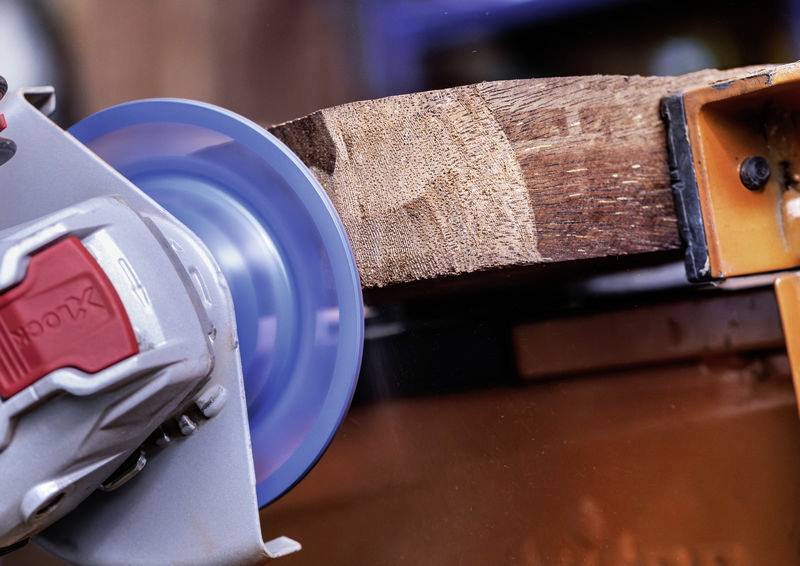 Ein elektrisches Schleifgerät glättet die Oberfläche eines Holzstücks. Das Holz ist teilweise abgeschliffen und zeigt eine glatte Textur.