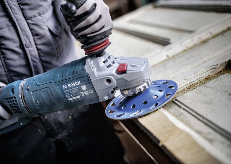 Eine Person schleift mit einem Bosch-Schleifgerät die Oberfläche eines Holzbalkens ab, um sie zu glätten.