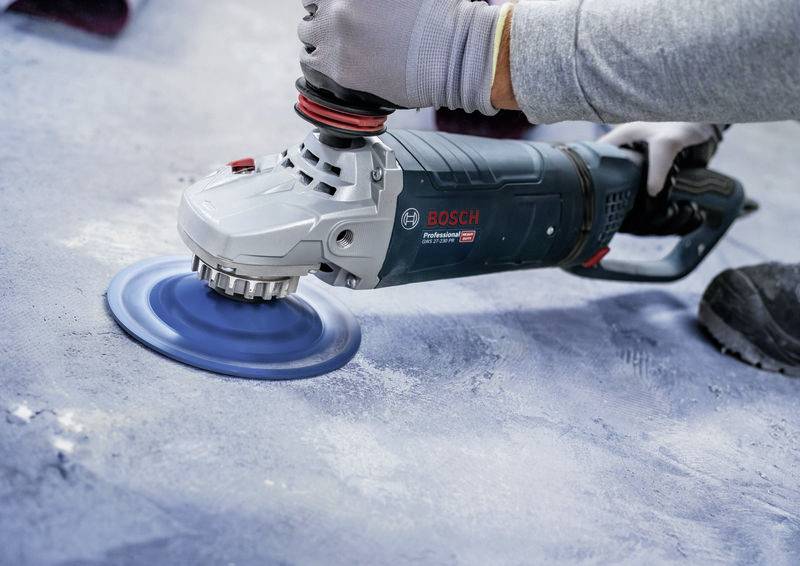Person schleift Oberfläche mit einer blauen Schleifmaschine. Nahaufnahme zeigt präzise Handhabung des Werkzeugs bei der Arbeit.