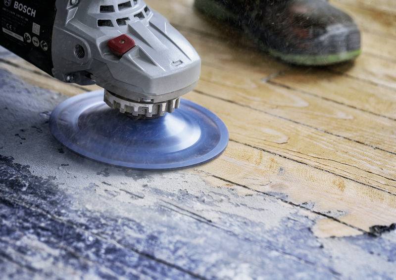Eine Person schleift mit einer elektrischen Schleifmaschine eine Holzoberfläche, um sie zu glätten. Sägemehl ist um das Werkzeug herum sichtbar.