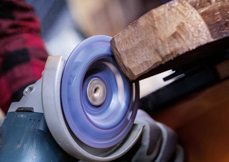 Eine Person schleift ein Holzstück mit einem elektrischen Schleifgerät. Nahaufnahme des rotierenden Schleifrades und des Holzes.