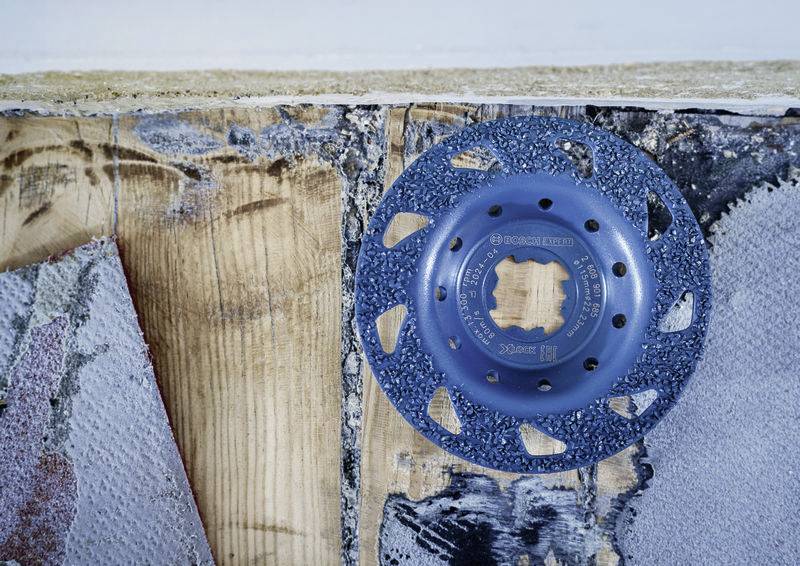 Ein blaues Schleifwerkzeug liegt auf einer grob bearbeiteten Holzoberfläche, umgeben von Schleifspuren und verschiedenen Materialien.