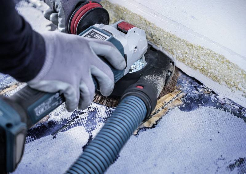 Person schleift mit einer elektrischen Schleifmaschine Farbe von einer Wand. Schutzbrille und Handschuhe werden getragen.