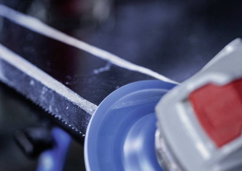 Nahaufnahme eines blauen Schleiftellers, der über eine Metalloberfläche mit bereits geschliffenen Kanten bewegt wird.