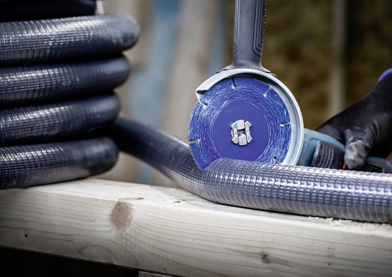 Eine Person schneidet mit einem Winkelschleifer ein Metallrohr, das auf einem Holztisch liegt. Der Hintergrund ist unscharf.