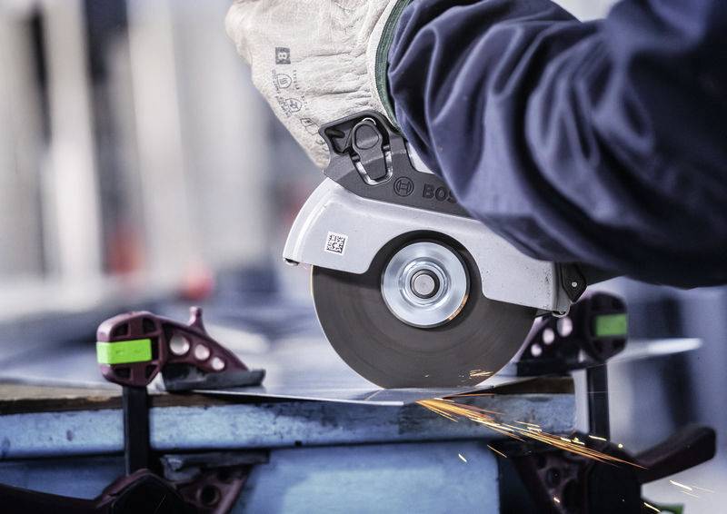 Eine Person schneidet Metall mit einer elektrischen Säge, Funken sprühen. Trägt Arbeitshandschuhe, Metallklemmen fixieren das Werkstück.