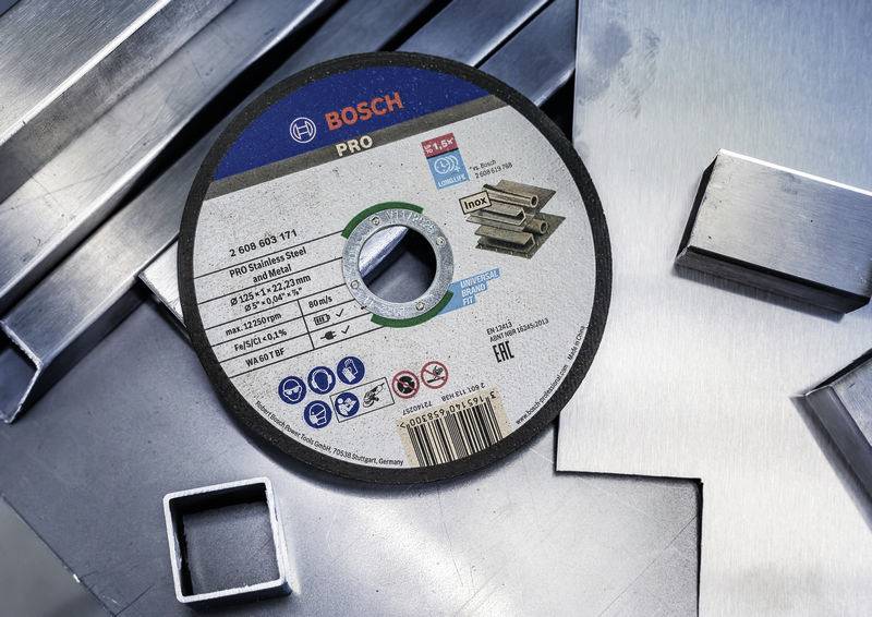 Schleifscheibe von Bosch Pro, liegt auf gestapeltem Metall. Etikett zeigt Spezifikationen: Durchmesser, Materialtyp und Sicherheits-Symbole.