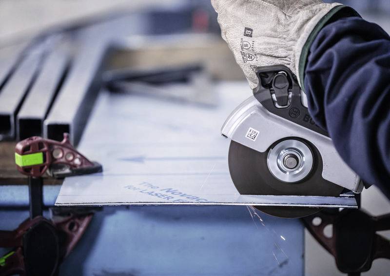 Eine Person schneidet mit einer elektrischen Metallsäge ein Blech, wobei Funken sprühen. Handschuh schützt die Hand des Bedieners.