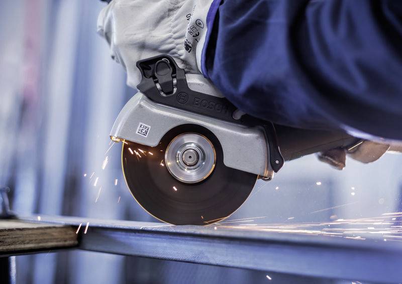 Eine Person schneidet mit einem Winkelschleifer Metall, während Funken fliegen. Nahaufnahme der Arbeitsaktion in einer Werkstatt.