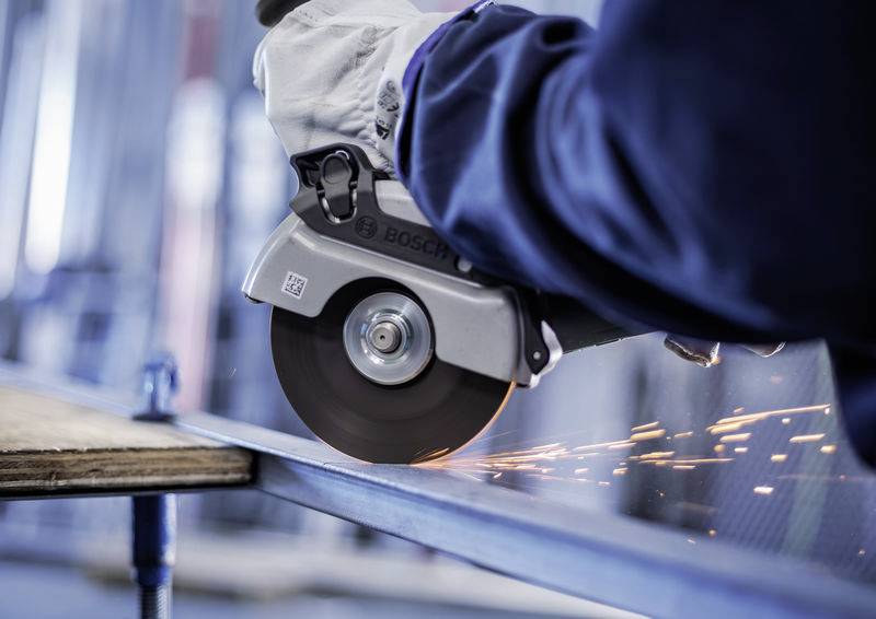 Eine Person schneidet mit einer elektrischen Trennschleifmaschine ein Metallstück, Funken fliegen.