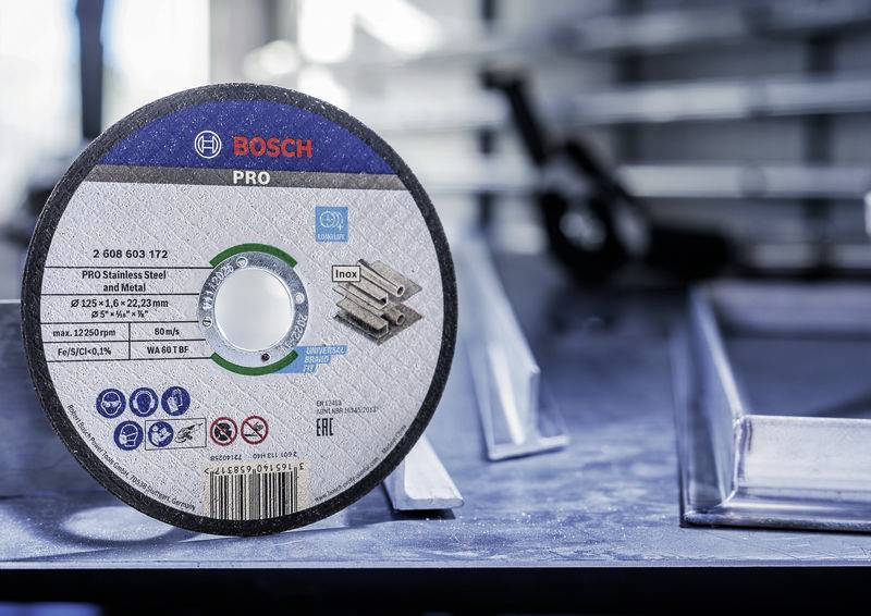 Schleifscheibe mit Aufschrift 'BOSCH PRO' und 'Inox' liegt auf einem Tisch neben Metallprofilen in einer Werkstattumgebung.