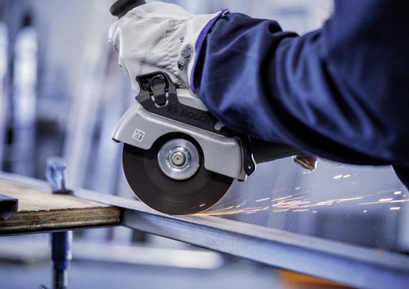 Eine Person in Schutzkleidung bedient eine Winkelschleifmaschine und schneidet Metall, Funken fliegen. Tätigkeitskontext Industriemontage.