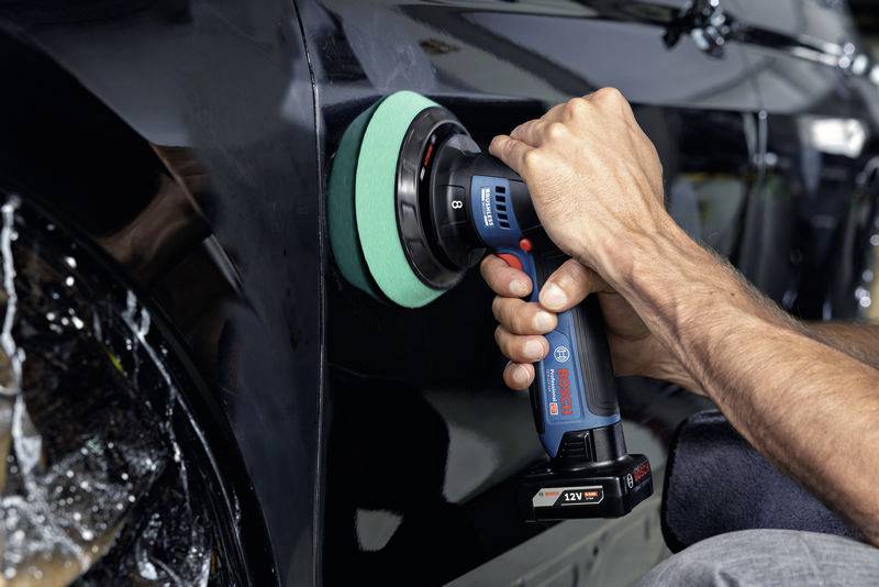 Eine Person poliert den Lack eines schwarzen Autos mit einer elektrischen Poliermaschine. Das Auto glänzt durch die Behandlung.