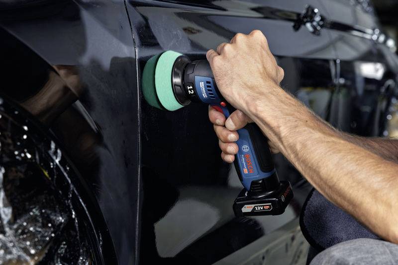 Ein Detailbild zeigt eine Person, die mit einer Poliermaschine den glänzenden Lack eines schwarzen Autos auf Hochglanz poliert.