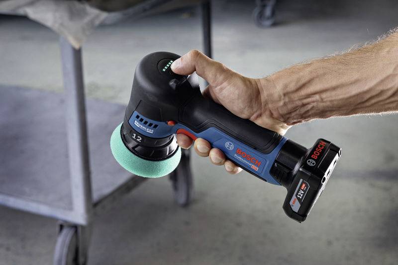 Ein Akku-Polierer wird von einer Hand gehalten. Er trägt das Markenlogo 'Bosch' und wird in einer Werkstatt verwendet.