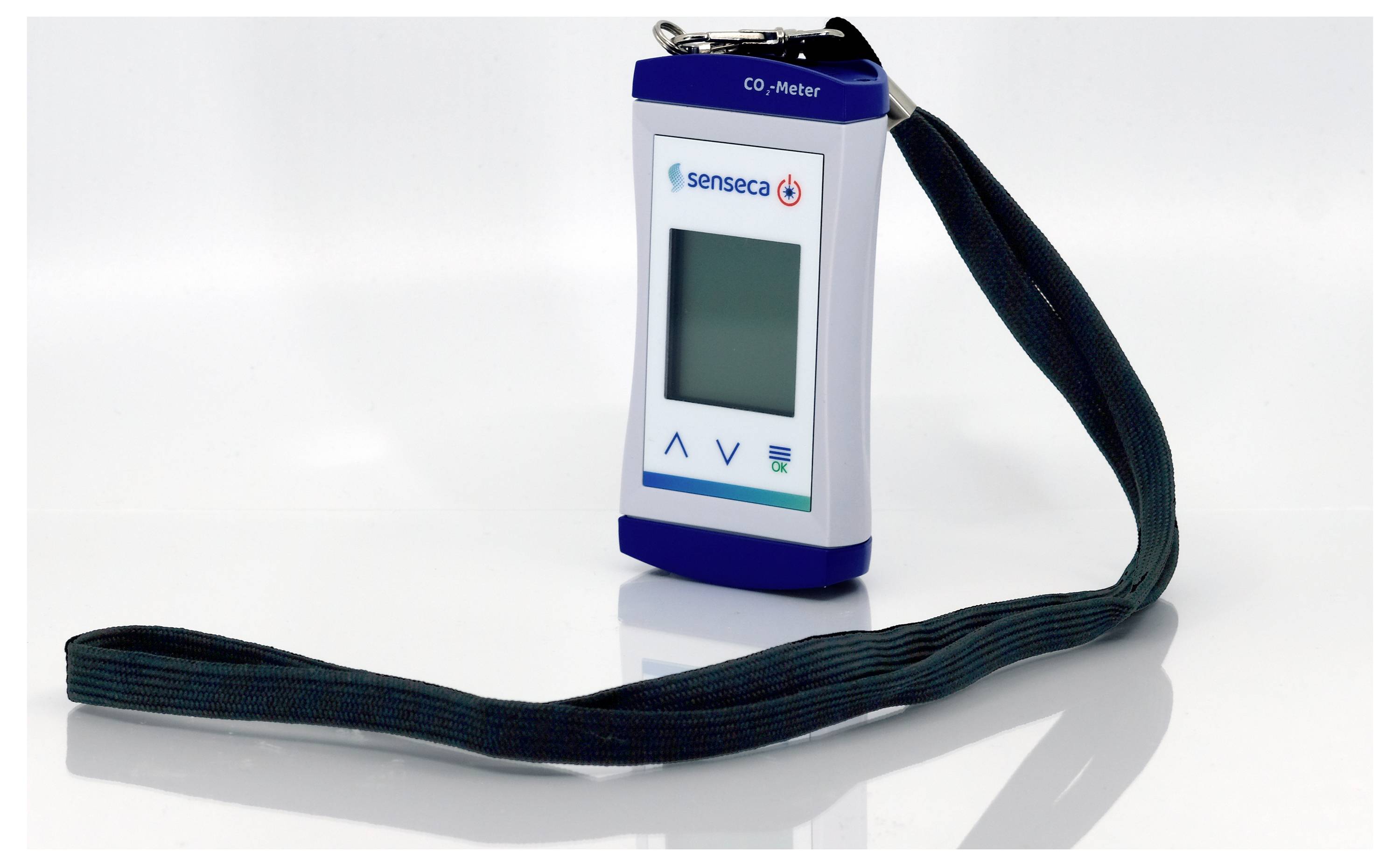 Ein tragbares CO2-Messgerät mit digitaler Anzeige und Navigationstasten, an einer dunklen Trägerschnur befestigt, mit der Markenbezeichnung 'senseco'.