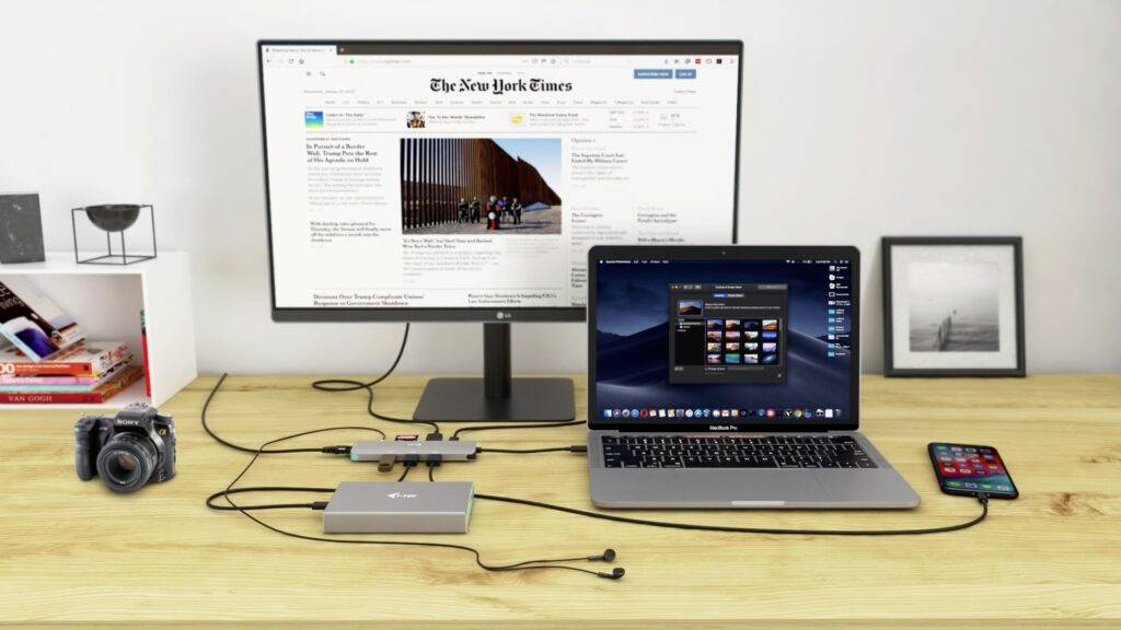 Ein Schreibtisch mit einem Laptop, angeschlossen an einen Monitor, der 'The New York Times' zeigt. Daneben eine Kamera und ein Smartphone.
