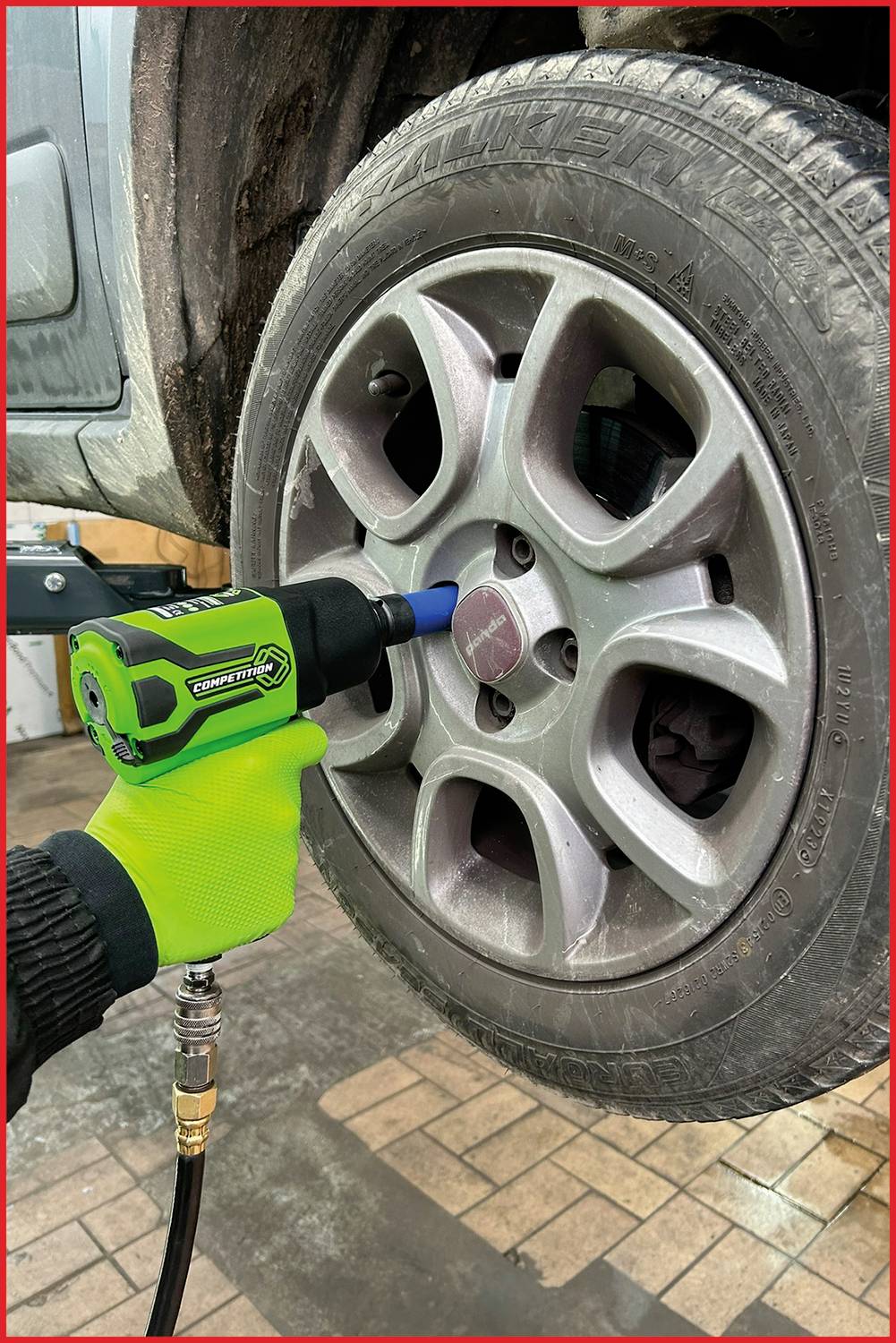 Eine Person benutzt einen grünen Schlagschrauber, um die Radschrauben eines schwarzen Autoreifens in einer Werkstatt zu befestigen.