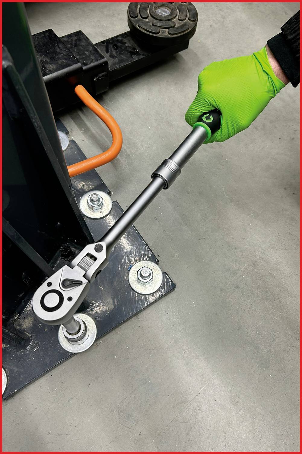 Eine Person mit grünem Handschuh benutzt einen Drehmomentschlüssel, um eine große Schraube an einer Maschine zu befestigen.