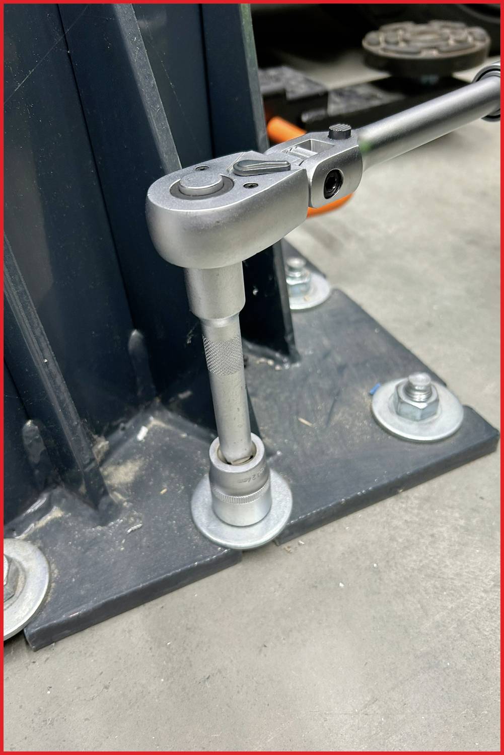 Umschaltknarre zieht Schraube an, befestigt ein Metallgestell auf Betonboden mit Muttern.