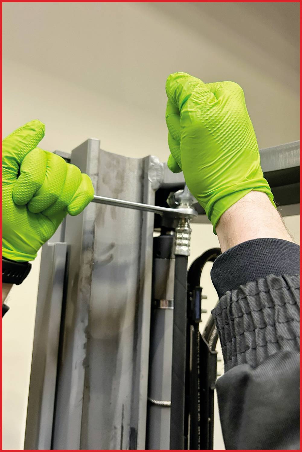 Eine Person mit grünen Handschuhen hält ein Werkzeug und arbeitet an einer Metallstruktur, vermutlich bei einer Reparatur oder Montage.