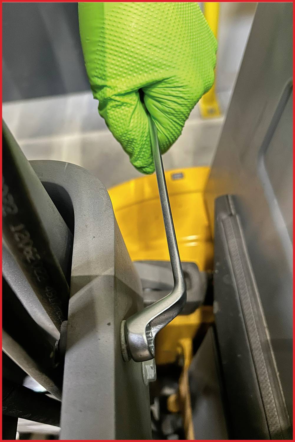 Hand mit grünem Handschuh hält einen Schraubenschlüssel, der an einer Metallmaschinenkomponente in einer industriellen Umgebung arbeitet.