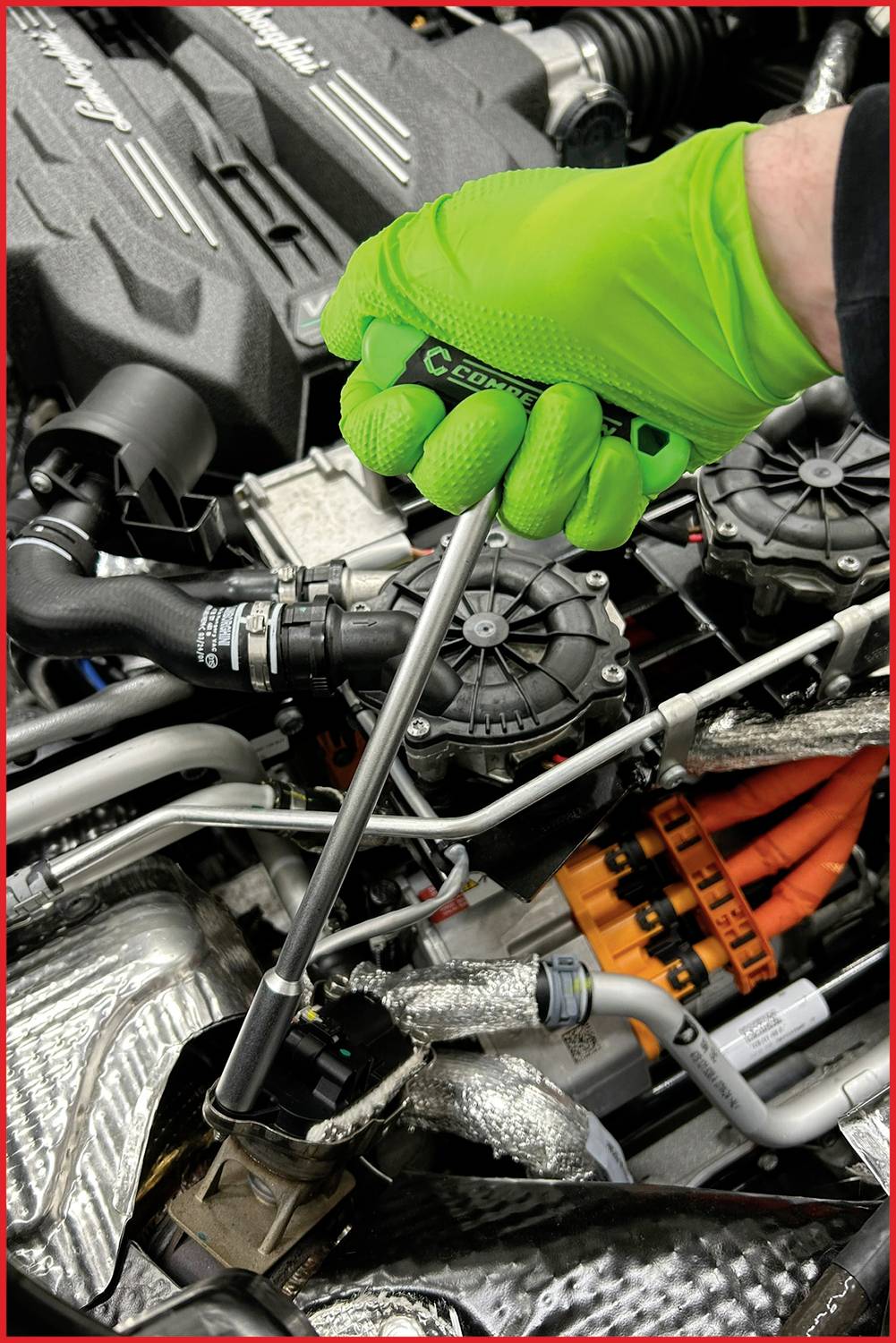 Eine Person mit grünen Handschuhen arbeitet mit einem Schraubenschlüssel an einem Motor. Sichtbare Kabel und Schläuche im Motorraum.